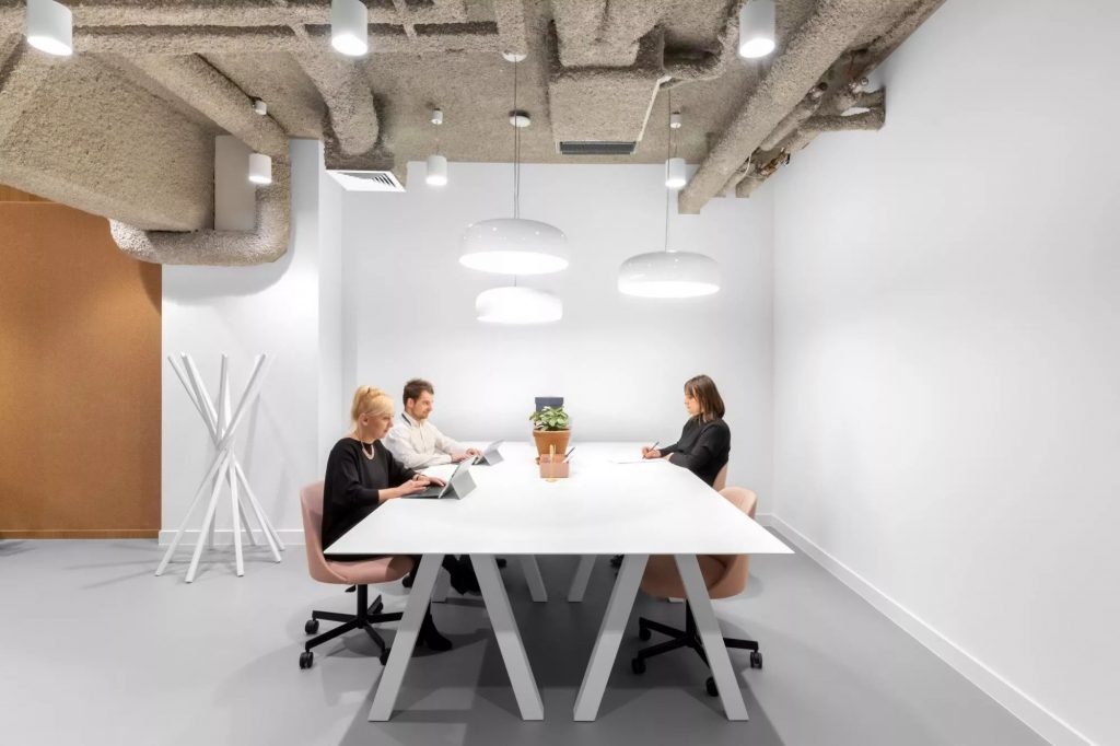 People sitting at a large white table inside the office at Spaces Fabryka Kart 
