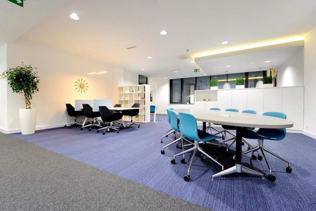 Bright workspace featuring white walls, purple carpet, blue chairs and working desks